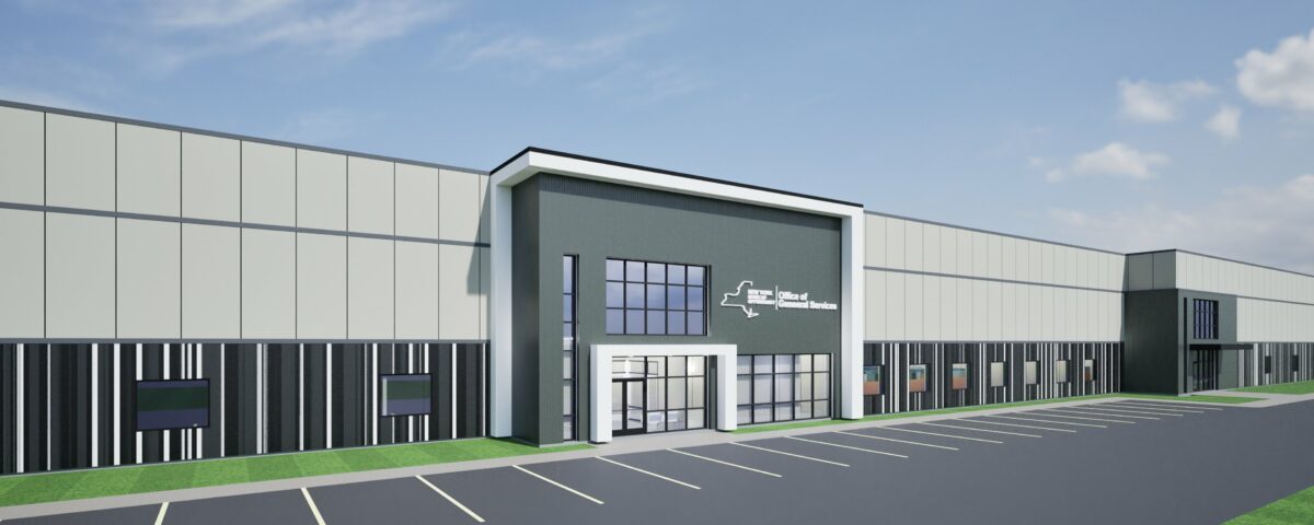Large, horizontal building in shades of gray with the words: New York State: Office of General Services on it in white. Building set against a blue sky with a few clouds and in an empty parking lot with a few areas of grass.