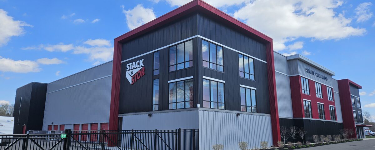 Climate Controlled Self Storage building in Rotterdam New York. Photographed on a sunny day with blue sky and white clouds. Stak N Stor logo on side of building. Building has light and dak gray materials with red accents.