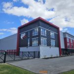 Climate Controlled Self Storage building in Rotterdam New York. Photographed on a sunny day with blue sky and white clouds. Stak N Stor logo on side of building. Building has light and dak gray materials with red accents.