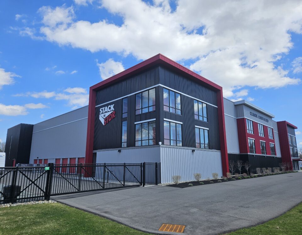 Climate Controlled Self Storage building in Rotterdam New York. Photographed on a sunny day with blue sky and white clouds. Stak N Stor logo on side of building. Building has light and dak gray materials with red accents.