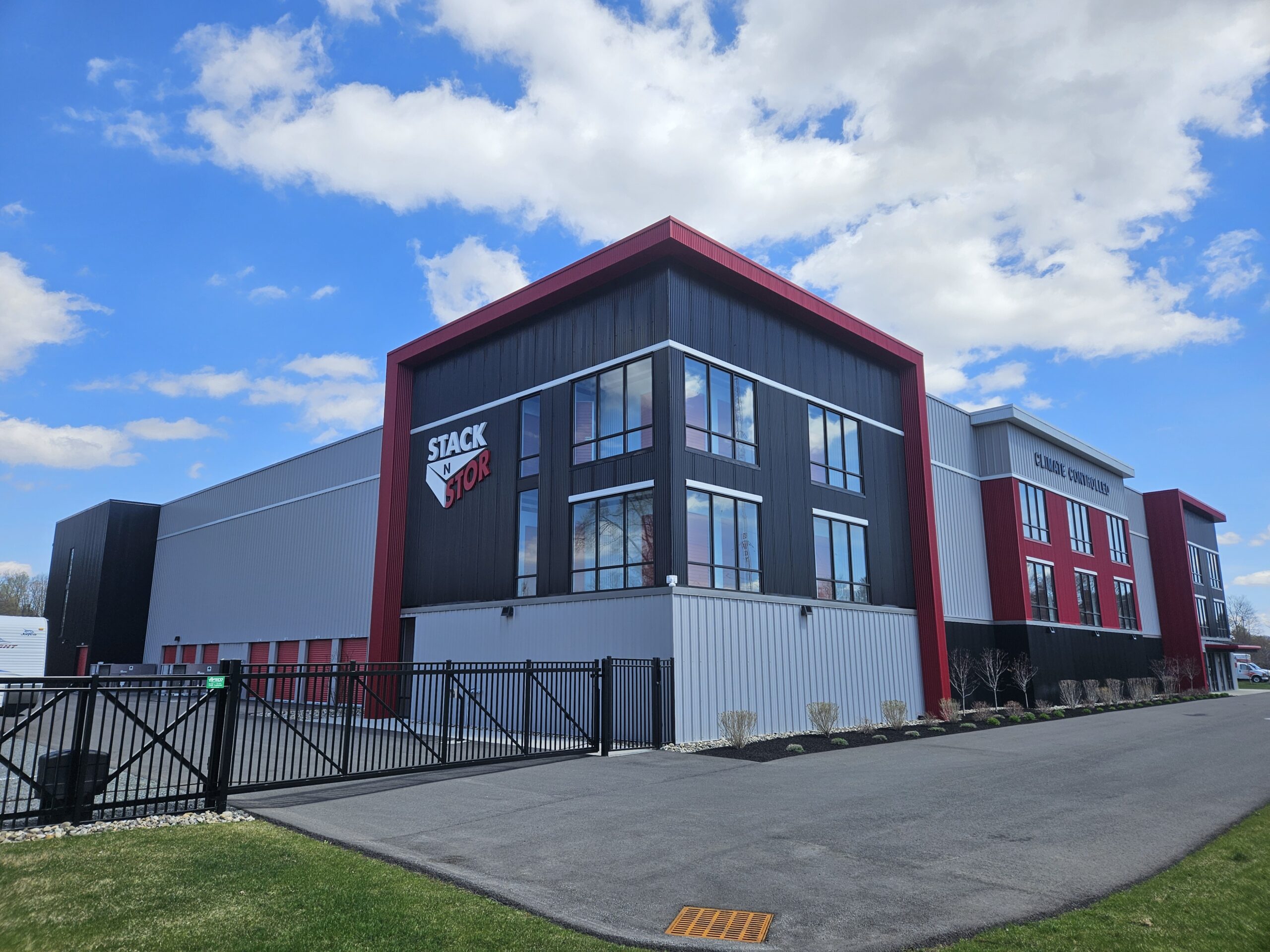 Climate Controlled Self Storage building in Rotterdam New York. Photographed on a sunny day with blue sky and white clouds. Stak N Stor logo on side of building. Building has light and dak gray materials with red accents.