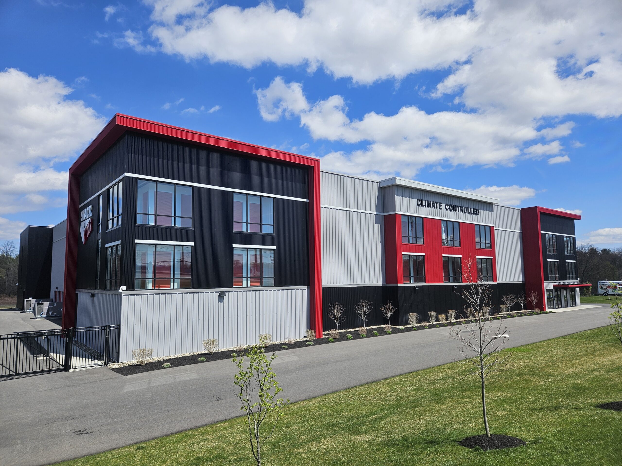 Climate Controlled Self Storage building in Rotterdam New York. Photographed on a sunny day with blue sky and white clouds. Stak N Stor logo on side of building. Building has light and dak gray materials with red accents.